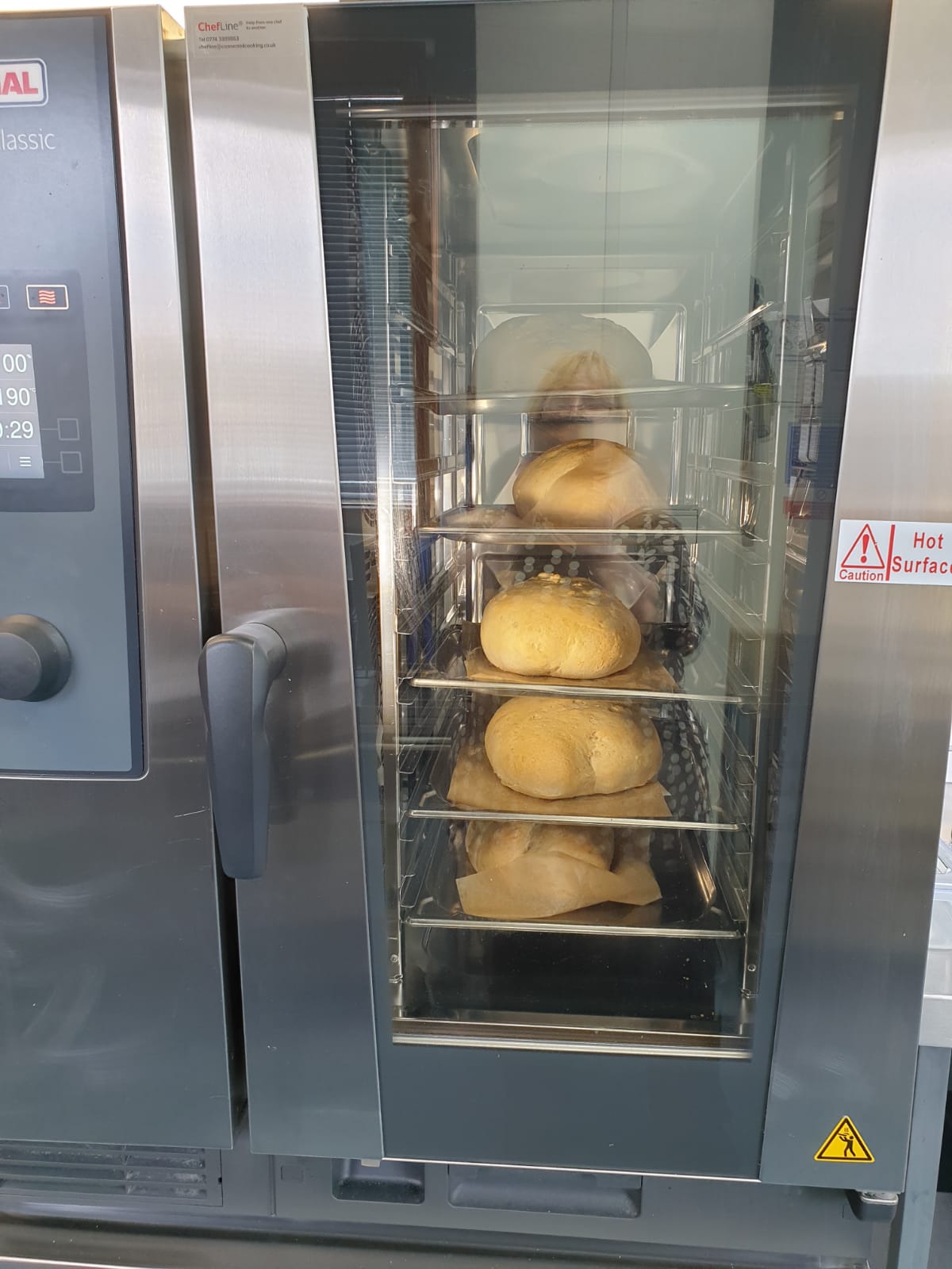 A tall catering oven with a glass door which shows the bread baking