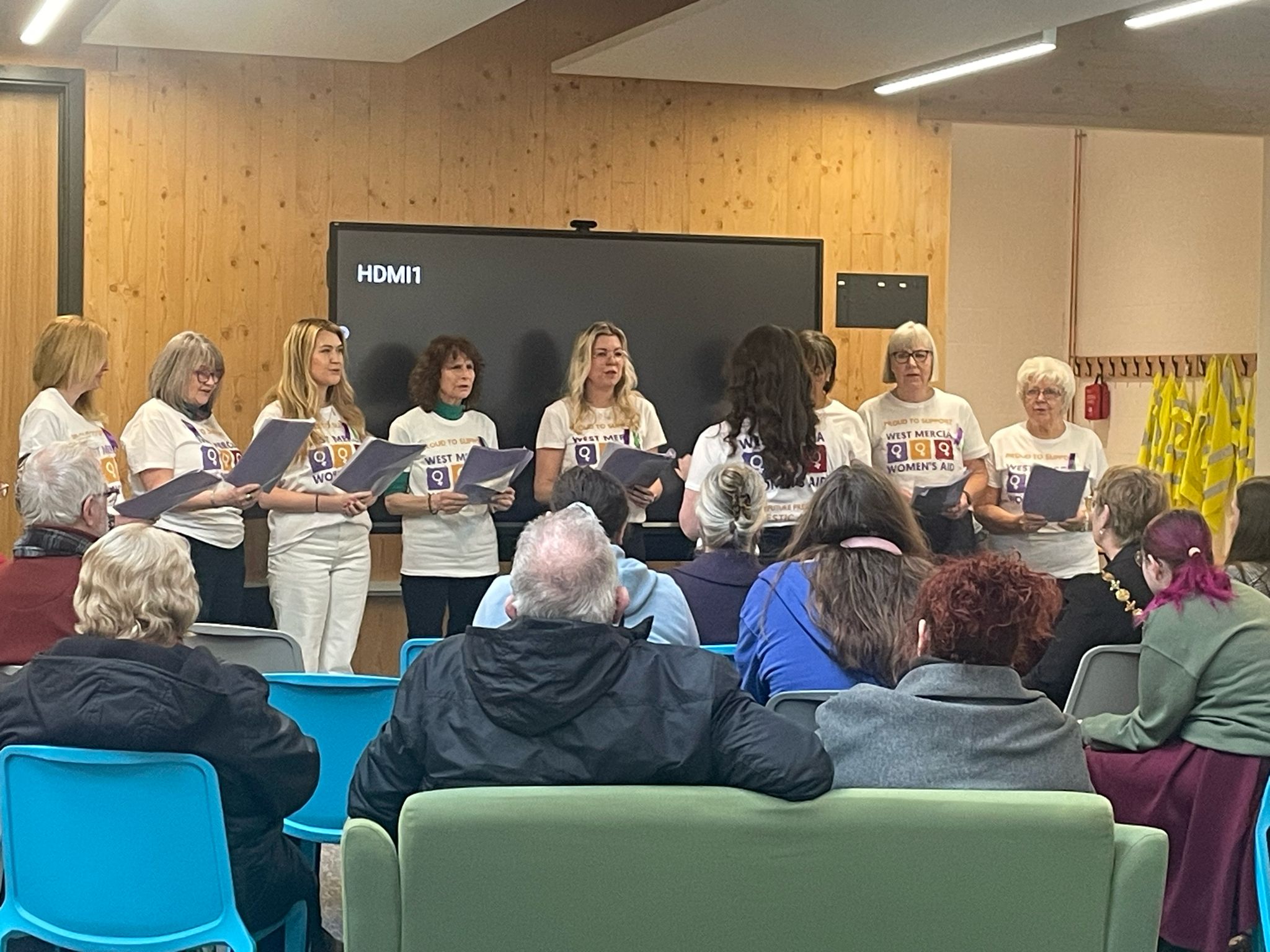 the Women's Aid Choir singing in front of a seated audience