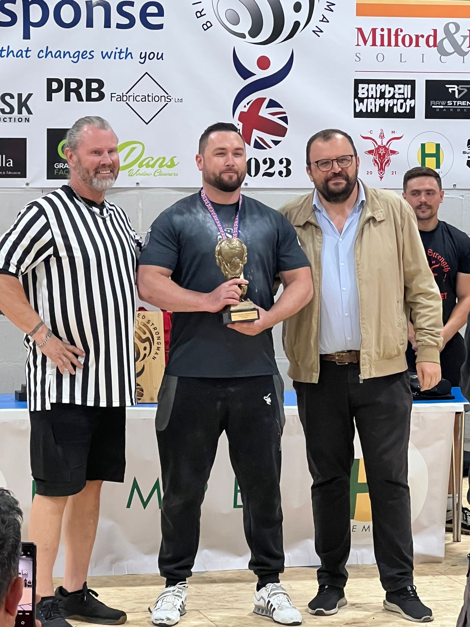 3 men standing in a row, one holds a trophy