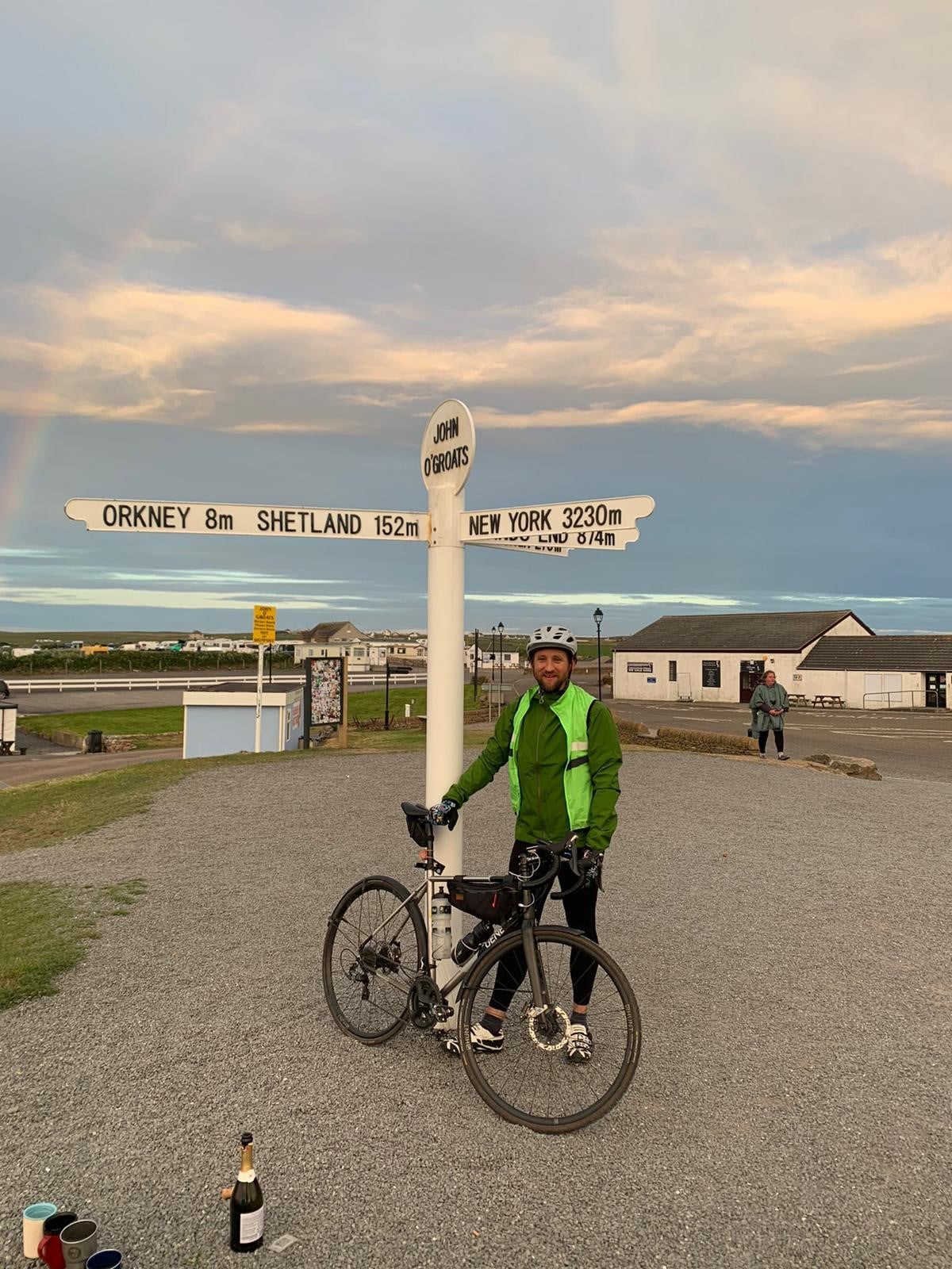 Andrew stands with his bike in front of the signpost that says Orkney 8m to the north and New York 3240 miles to the west in John O Groats