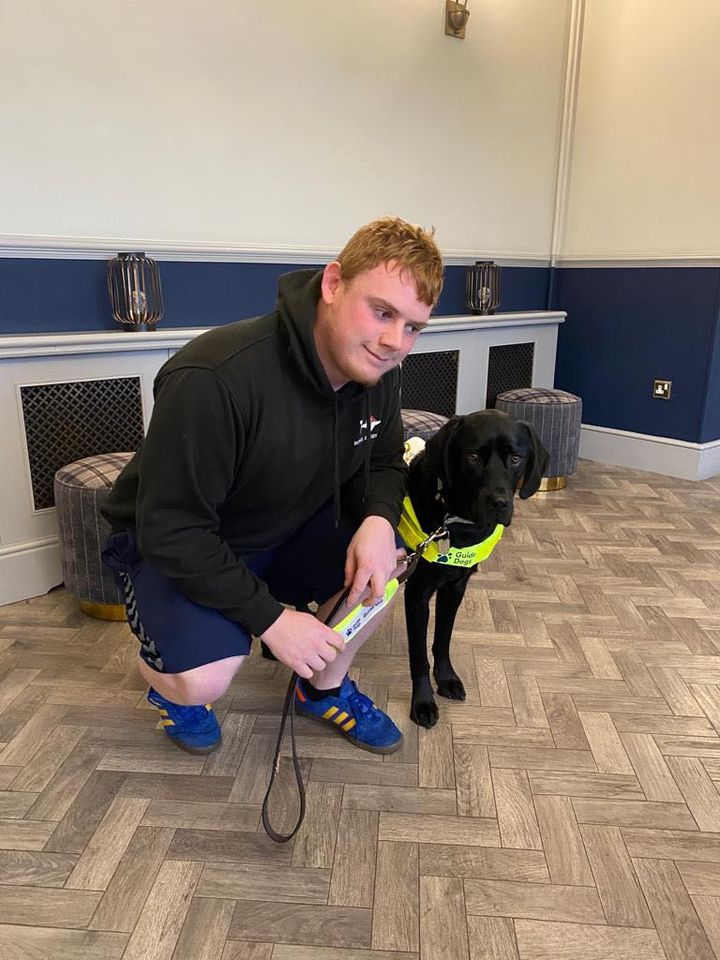 Chris crouches down next to Bracken a beautiful black Labrador standing to his left 