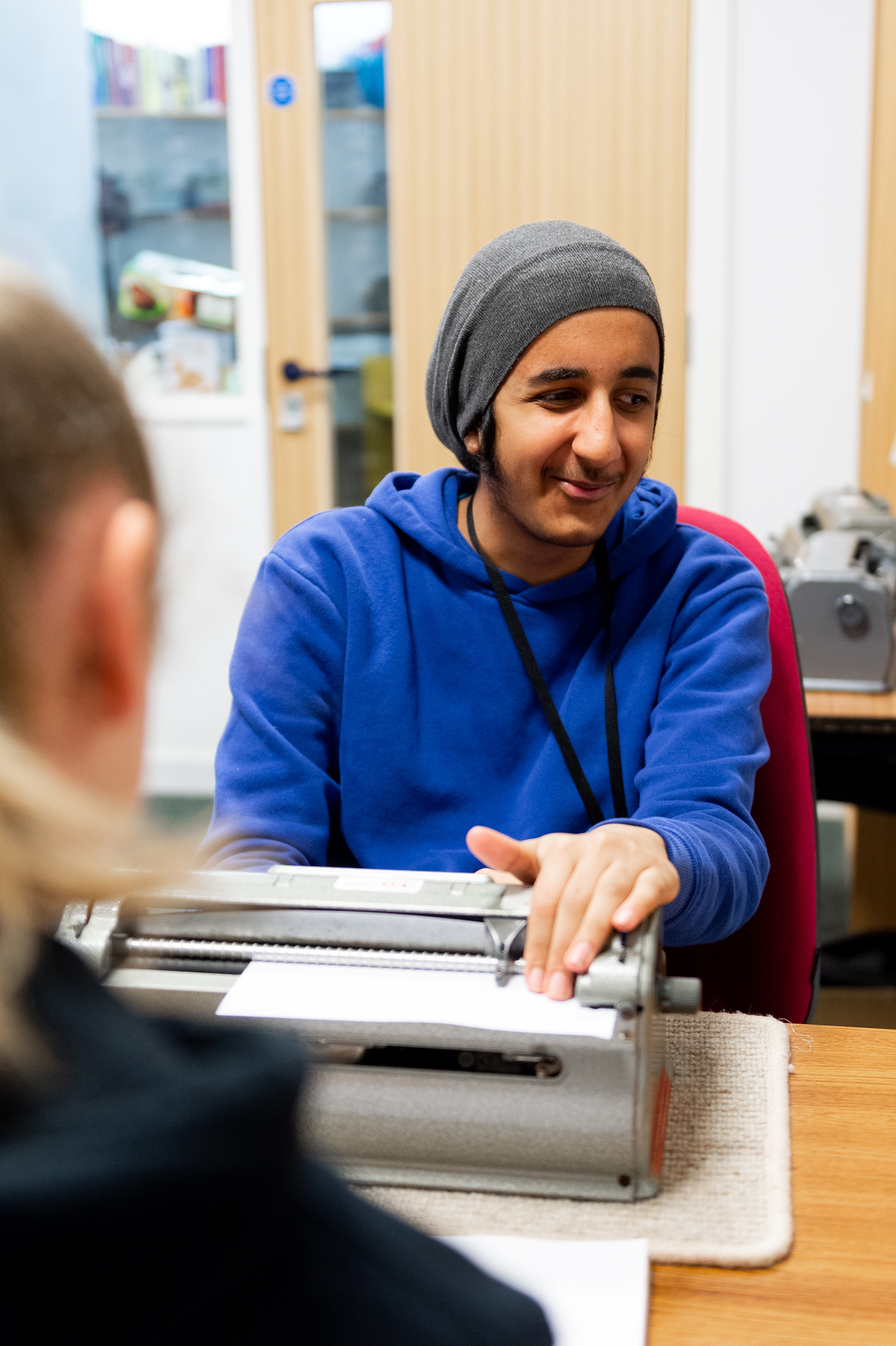 a male student working on a Perkins Brailler a female Braille teacher sits in front of him