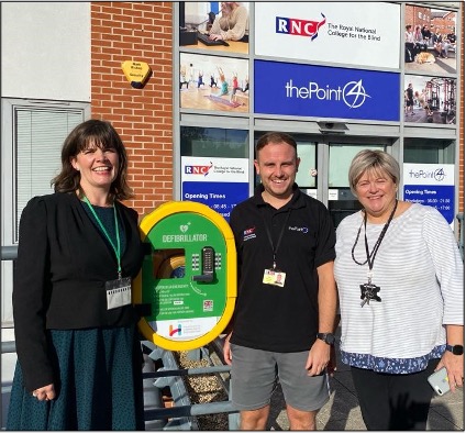 3 people stand around the defibrillator at the entrance to RNC and thePoint4