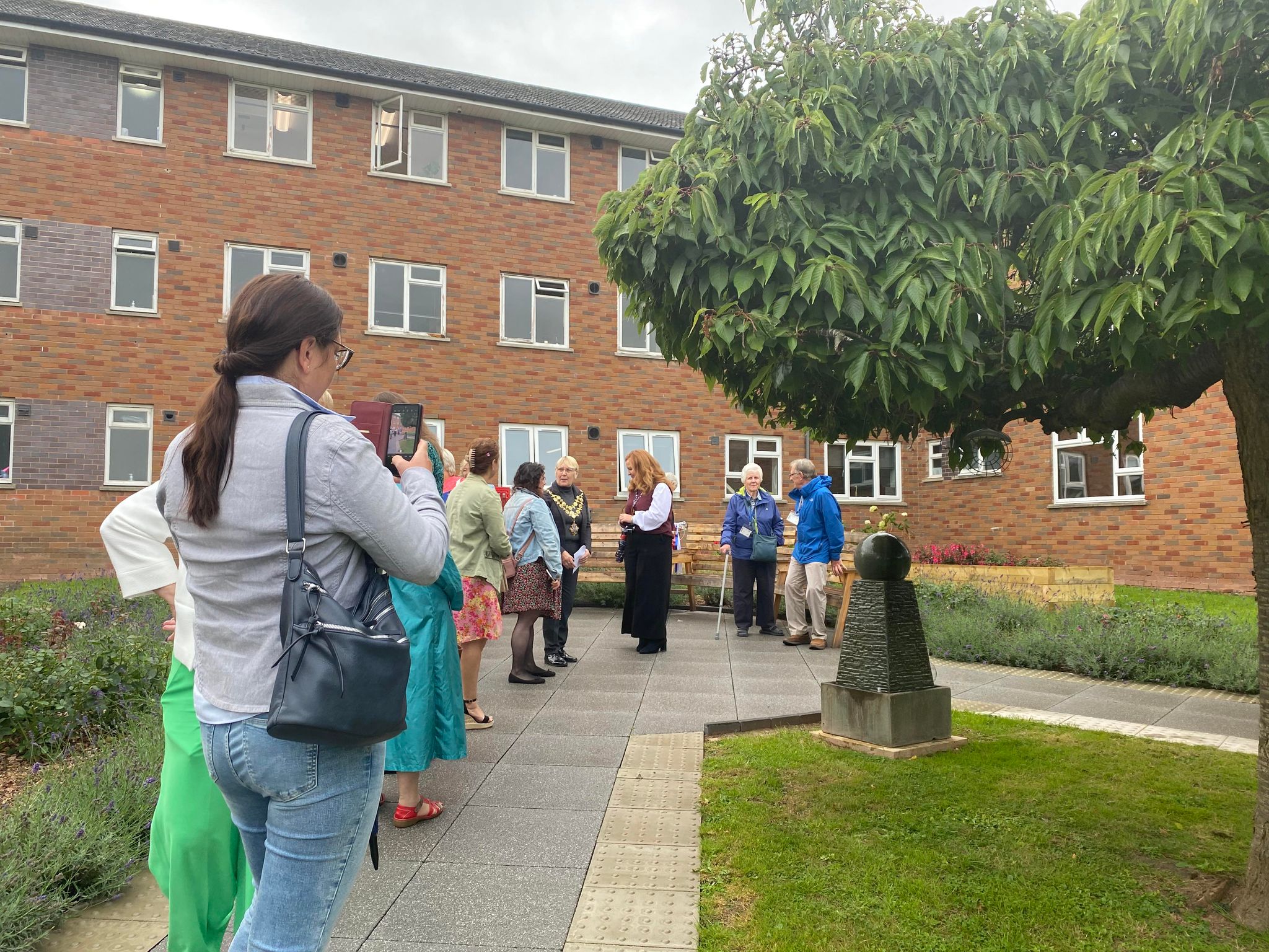 Visitors exploring the garden with the water feature and a tree in view