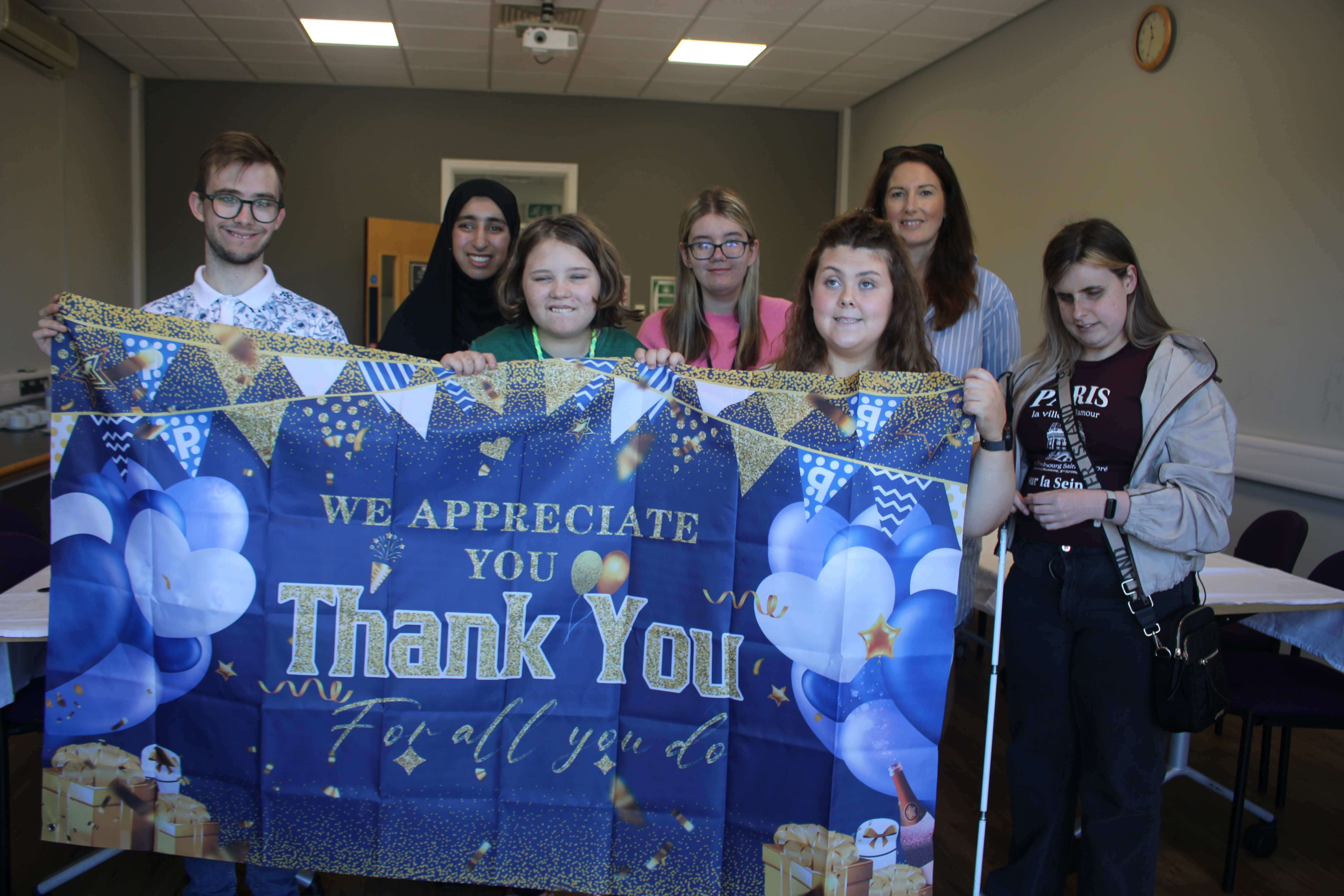 the group of students and their teacher holding up a banner which reads 'we appreciate yout hank you' 