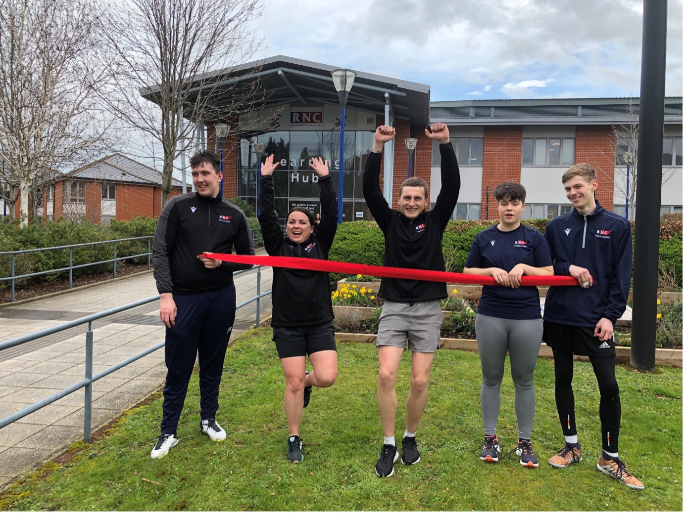 students and runners hold up a pretend finish line in front of the College