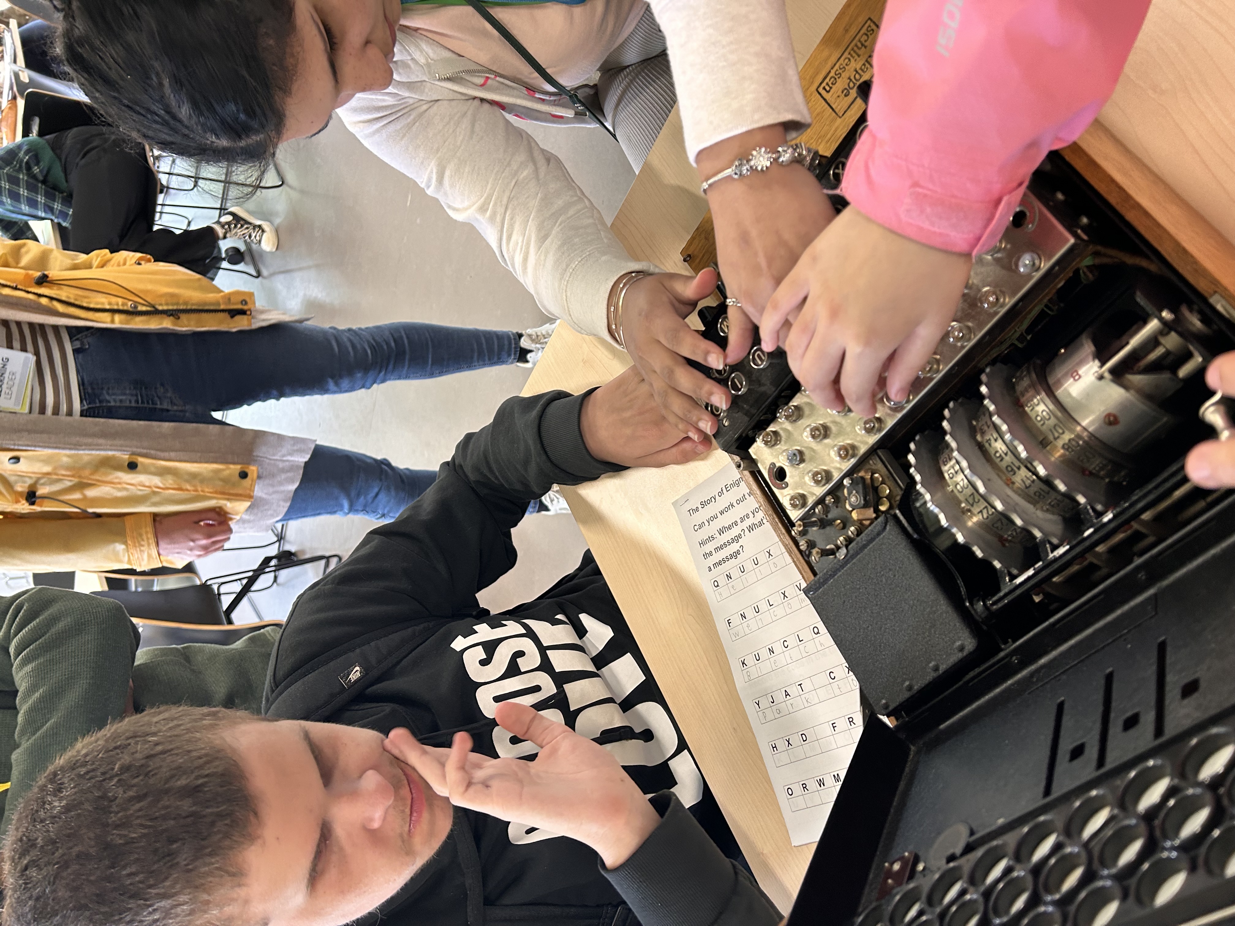 the hands of 3 students exploring the keys on the Enigma machine