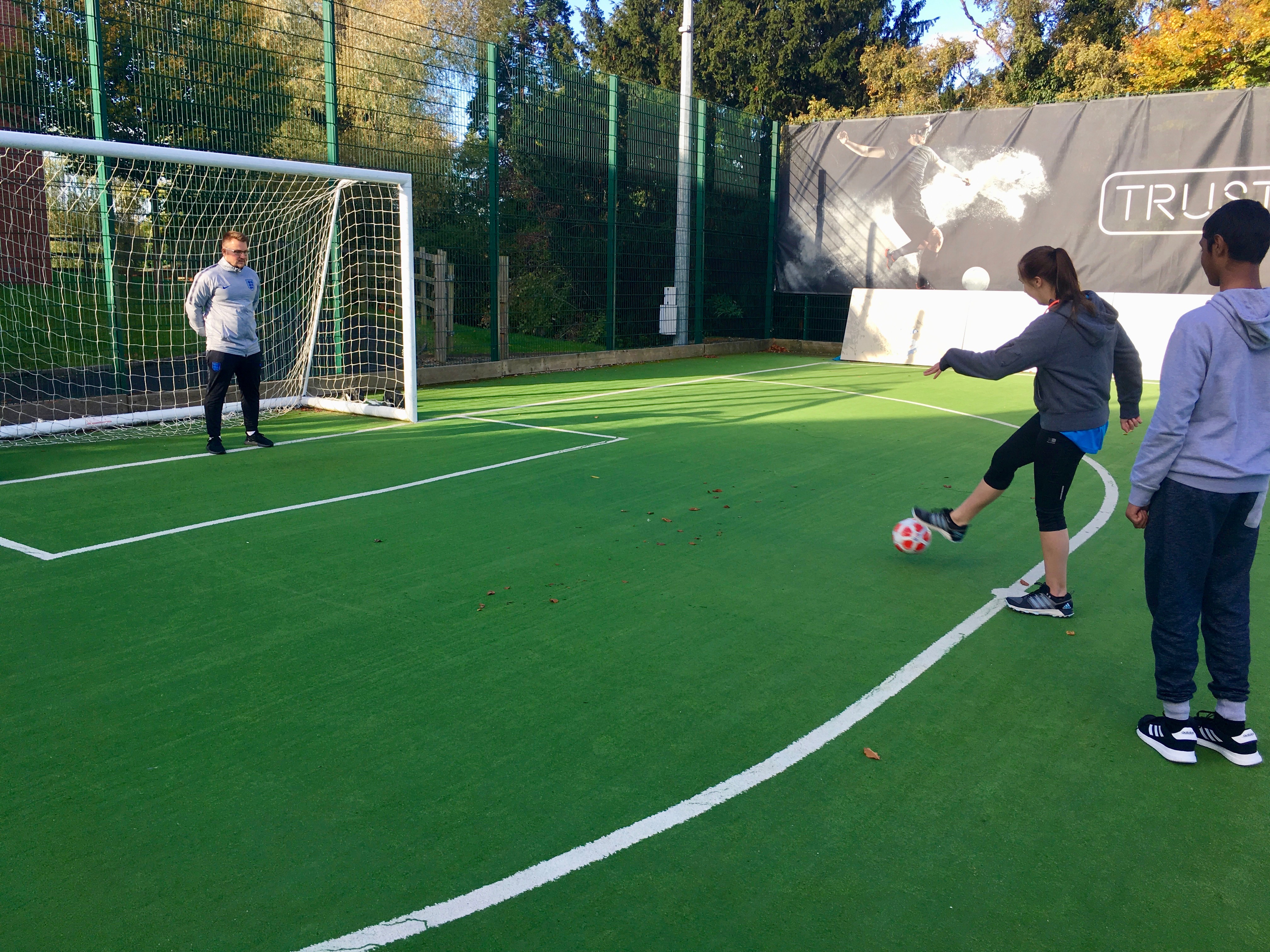 a female lines up with a ball ready to shout a penalty at the goal, a male goalkeeper takes position, there is one male spectator 