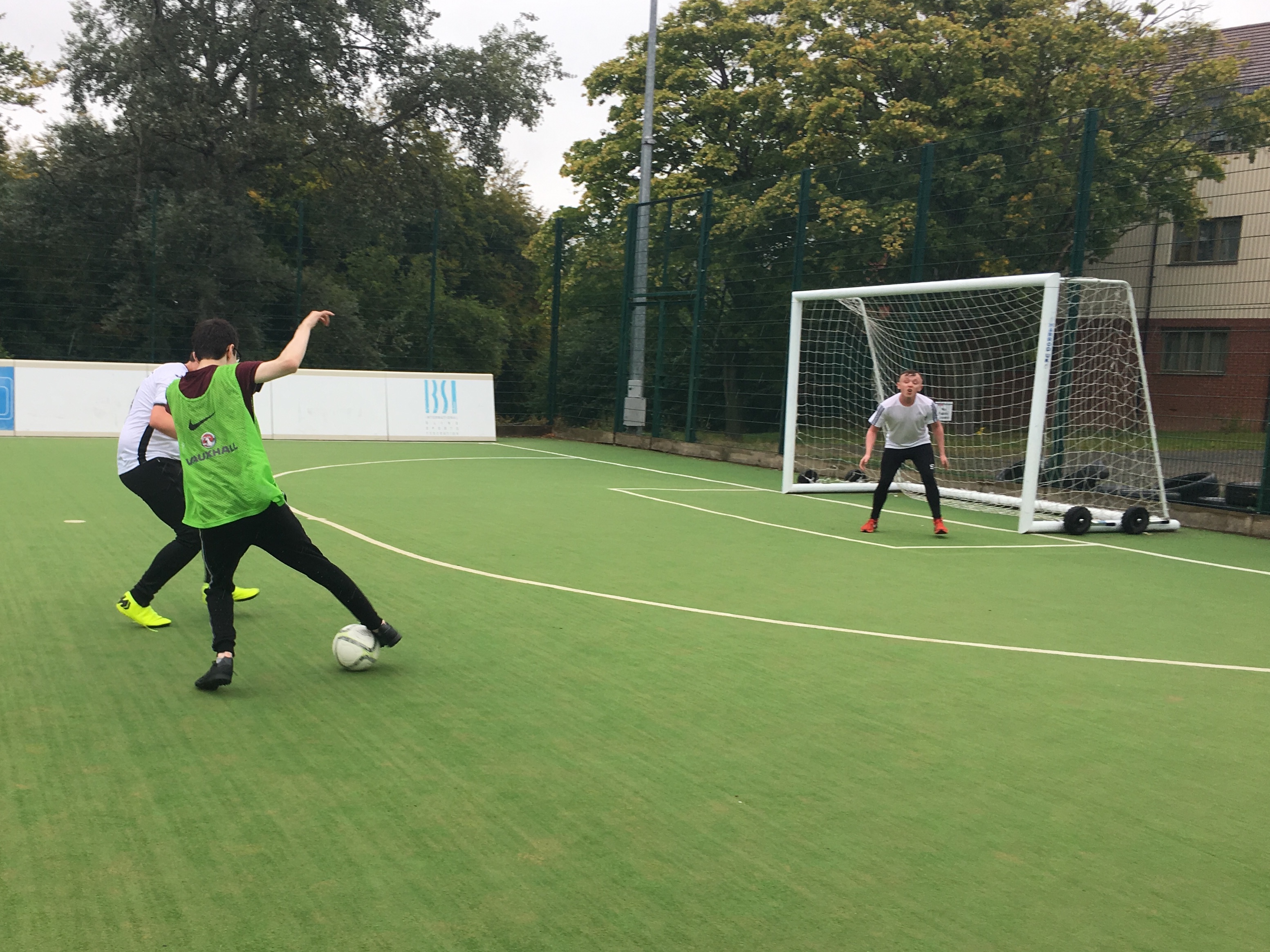 one male player tackles another in front of goal, the goalkeeper defends goal