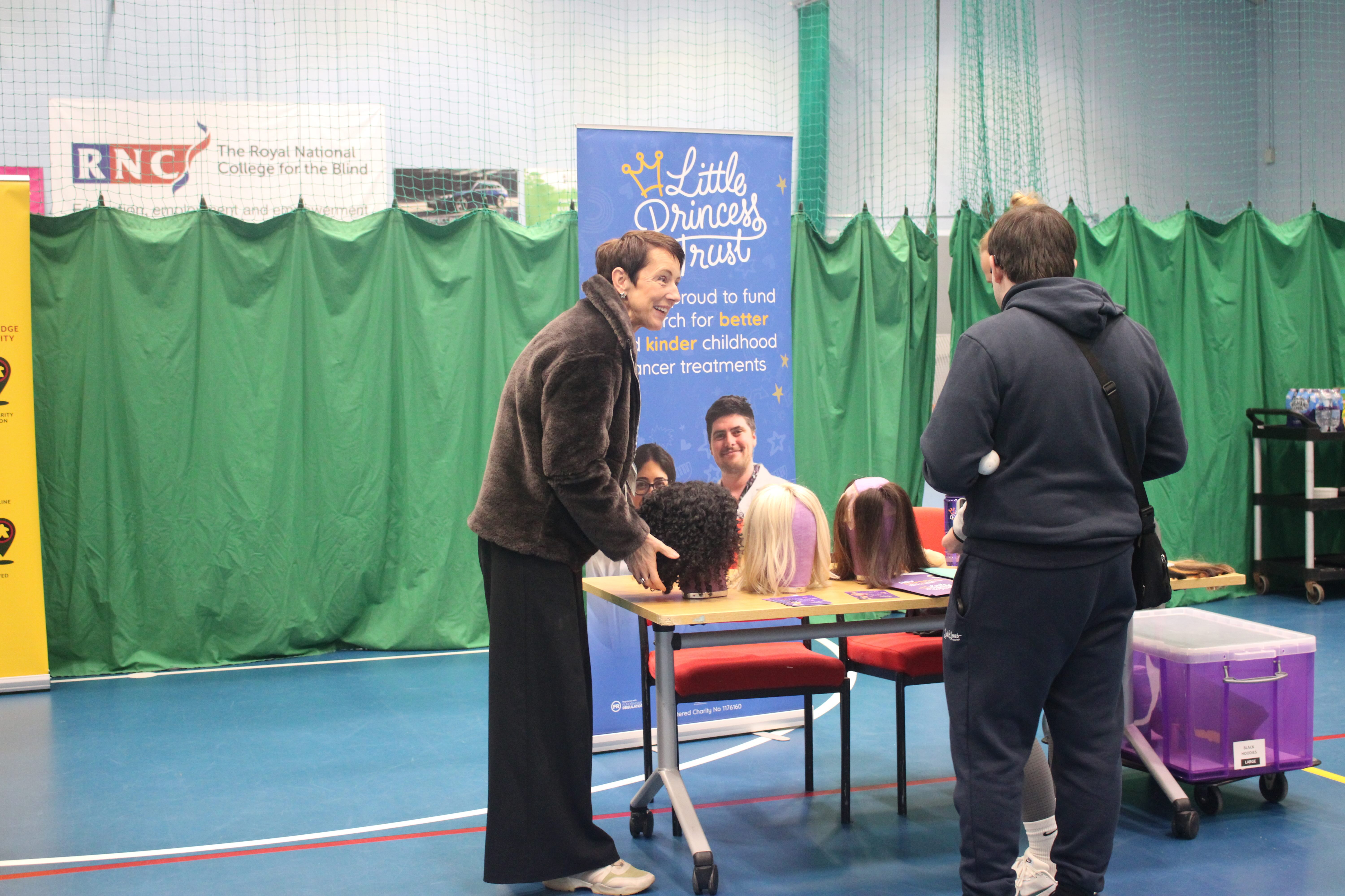 The LPT Trust stand with a table showcasing their wigs. A lady is talking to two visitors. The LPT purple banner is displayed by the table