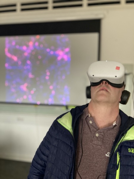A man looking upwards wearing large white virtual reality goggles 