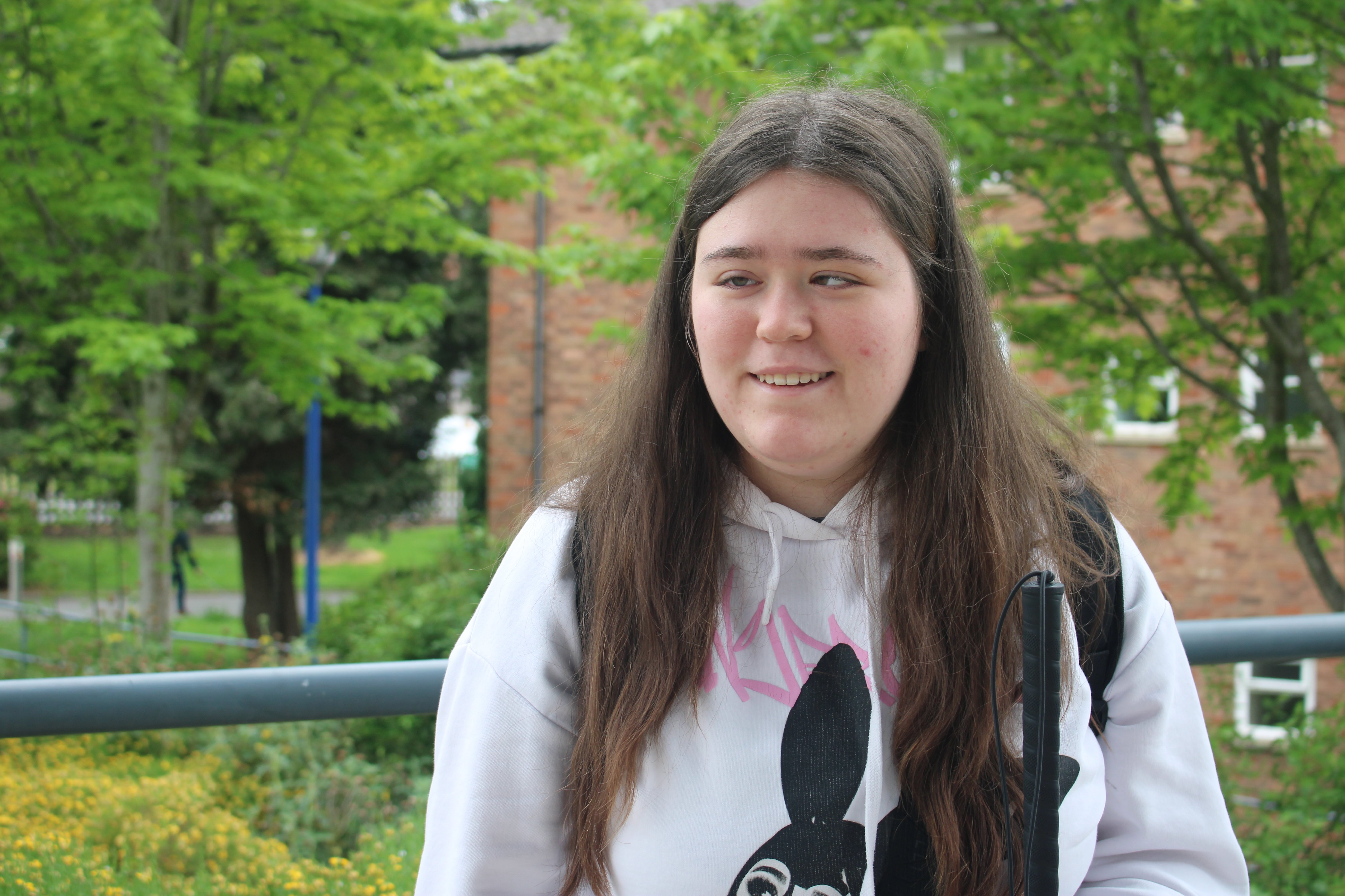 a picture of Vasilisa smiling - she is standing outside with shrubbery behind her