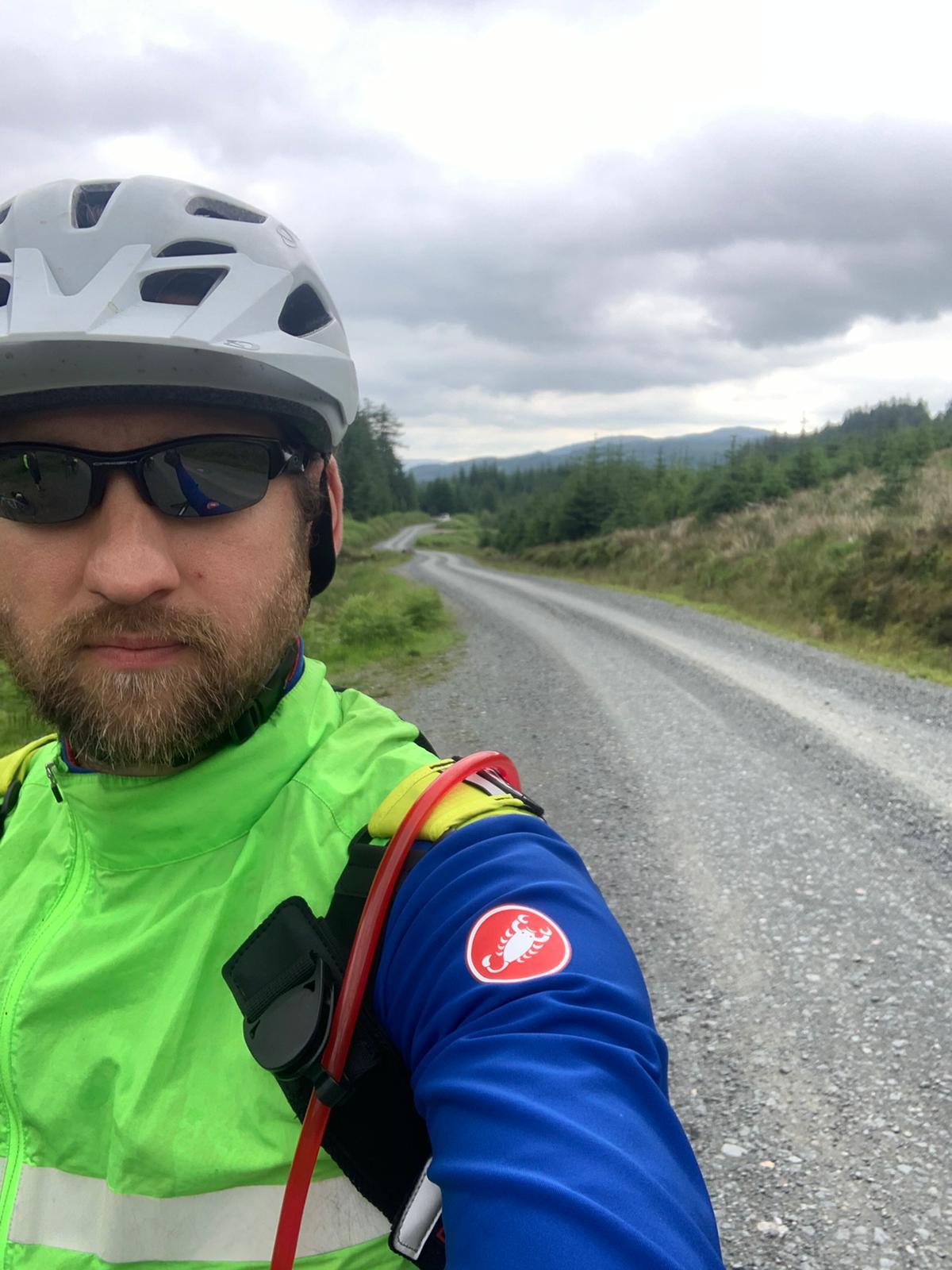 A selfie with a winding road and mountains and greenery in the background